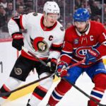 Ottawa Senators captain Brady Tkachuk (left, white jersey) and Montreal Canadiens captain Nick Suzuki (right, red jersey) battle intensely with their sticks for control of the puck along the arena boards during an NHL game.
