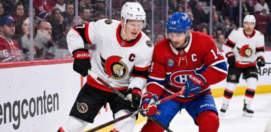 Ottawa Senators captain Brady Tkachuk (left, white jersey) and Montreal Canadiens captain Nick Suzuki (right, red jersey) battle intensely with their sticks for control of the puck along the arena boards during an NHL game.