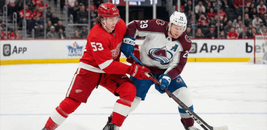Avalanche vs Red Wings TV Schedule: Why You Can’t Miss This Saturday Matinee Clash Detroit Red Wings defenseman Moritz Seider (53) in a red home jersey and Colorado Avalanche forward Nathan MacKinnon (29) in a white and maroon away jersey battle fiercely for the puck along the boards during an NHL game at Little Caesars Arena.