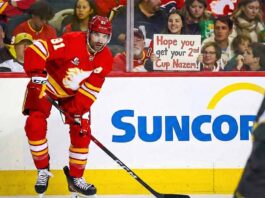 Report: Nazem Kadri ‘Open’ to Trade as 4 Teams Emerge as Frontrunners Calgary Flames center Nazem Kadri (#91) skating on the ice during a game, looking towards the camera. Behind the glass in the background, a smiling fan holds up a handwritten sign that reads, "Hope you get your 2nd Cup Nazem!"
