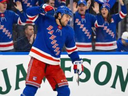 New York Rangers player Kiefer Sherwood, wearing number 44, pumps his fist and yells in celebration on the ice during a game. Fans wearing Rangers jerseys cheer behind the glass, and a Jameson Irish Whiskey advertisement is visible on the boards.