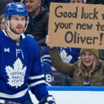 Is Oliver Ekman-Larsson Worth a First-Round Pick? The Latest Leafs Trade Buzz Toronto Maple Leafs defenseman Oliver Ekman-Larsson (95) is on the ice during a game, while in the background, a smiling female fan holds a cardboard sign that reads, "Good luck with your new team Oliver!".