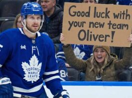 Is Oliver Ekman-Larsson Worth a First-Round Pick? The Latest Leafs Trade Buzz Toronto Maple Leafs defenseman Oliver Ekman-Larsson (95) is on the ice during a game, while in the background, a smiling female fan holds a cardboard sign that reads, "Good luck with your new team Oliver!".