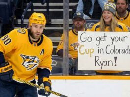 The Heartbreaking Decision Facing the Nashville Predators and Ryan O’Reilly Nashville Predators alternate captain Ryan O'Reilly (90) stands on the ice looking forward. Behind the glass barrier, a smiling female fan in a Predators jersey and beanie holds up a white poster sign with handwritten text that reads, "Go get your Cup in Colorado Ryan!".