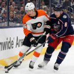 Philadelphia Flyers forward Trevor Zegras (#46) in a white away jersey and Columbus Blue Jackets defenseman Zach Werenski (#8) in a navy home jersey battle for a loose puck against the boards during an NHL game at Nationwide Arena.