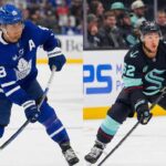 Is This the Blockbuster That Finally Fixes the Leafs? Kypreos Targets Kraken Duo A split photograph featuring two NHL players on the ice during respective games. On the left side, Toronto Maple Leafs forward William Nylander wears a blue No. 88 jersey and skates with the puck. On the right side, Seattle Kraken defenseman Brandon Montour wears a dark dark blue No. 62 jersey and is shown in a low skating stance.