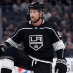 Why the Los Angeles Kings Trading for Steven Stamkos Makes Perfect Sense A mock-up concept image showing NHL forward Steven Stamkos wearing a black Los Angeles Kings home jersey and helmet, kneeling on the ice rink during a game setting.