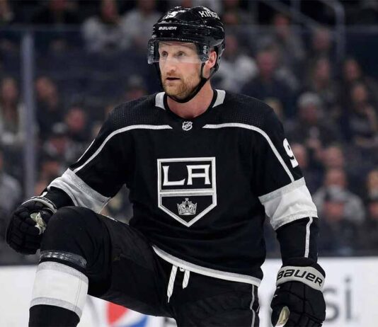 Why the Los Angeles Kings Trading for Steven Stamkos Makes Perfect Sense A mock-up concept image showing NHL forward Steven Stamkos wearing a black Los Angeles Kings home jersey and helmet, kneeling on the ice rink during a game setting.