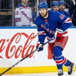 NY Rangers defenseman Vladislav Gavrikov (#44), currently the subject of intense trade rumors amid reports he is unhappy with the team's rebuild, skates with the puck past Coca-Cola and LEGO advertisements on the boards.