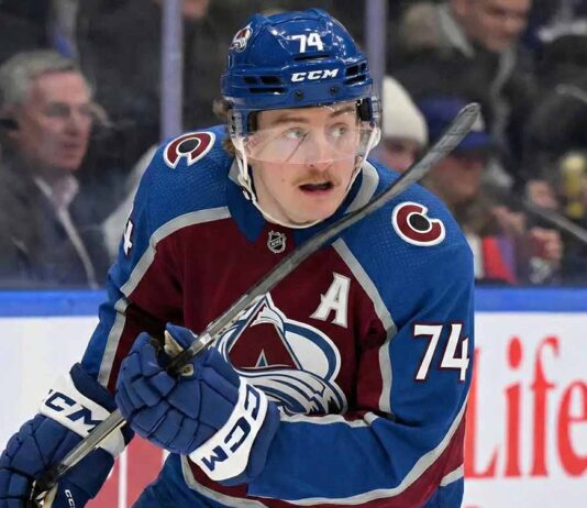 Colorado Avalanche forward Bobby McMann (74) looking up on the ice, wearing the team's maroon home jersey and a blue helmet during a game.