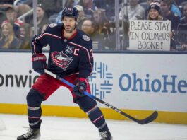 Boone Jenner Trade Rumors: The “U-Turn” That Could Haunt the Edmonton Oilers Columbus Blue Jackets captain Boone Jenner (#38) in a ready stance on the ice during a game. Behind the rink glass, a smiling female fan wearing a Blue Jackets jersey holds up a handmade white sign with blue text that reads, "Please stay in Columbus Boone!"