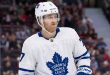 A photorealistic rendering of defenseman Dougie Hamilton standing on an ice hockey rink, wearing a white Toronto Maple Leafs away jersey with the blue Maple Leaf crest, blue gloves, and a white helmet bearing his number 7 and team decals.