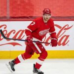 Detroit Red Wings defenseman Dougie Hamilton, wearing number 7, skates on the ice with his stick during a game, in front of a large Coca-Cola logo on the boards.