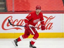 Detroit Red Wings defenseman Dougie Hamilton, wearing number 7, skates on the ice with his stick during a game, in front of a large Coca-Cola logo on the boards.