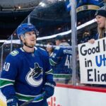 Vancouver Canucks center Elias Pettersson smiles as he looks up at a female fan pressing a handmade sign against the rink glass that reads "Good luck in Utah Elias." during pre-game warmups.