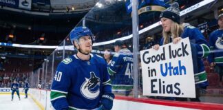 Vancouver Canucks center Elias Pettersson smiles as he looks up at a female fan pressing a handmade sign against the rink glass that reads "Good luck in Utah Elias." during pre-game warmups.