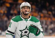 Vancouver Canucks forward Evander Kane pictured in a concept white Dallas Stars road uniform, wearing green and black Stars gloves and a white Bauer helmet with his mouthguard visible, looking upwards while standing on the ice.