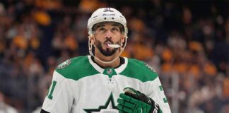 Vancouver Canucks forward Evander Kane pictured in a concept white Dallas Stars road uniform, wearing green and black Stars gloves and a white Bauer helmet with his mouthguard visible, looking upwards while standing on the ice.
