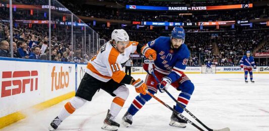 Will the Philadelphia Flyers Upset the New York Rangers Tonight? An action photograph from an NHL game showing Philadelphia Flyers forward Travis Konecny (left, in white #11 jersey) and New York Rangers center Mika Zibanejad (right, in blue #93 jersey) intensely battling for control of a loose puck on the ice.