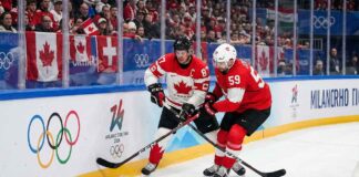 Team Canada captain Sidney Crosby (87) and Team Switzerland captain Roman Josi (59) battle fiercely for possession of the puck along the boards during a preliminary round men's hockey game at the 2026 Milano Cortina Winter Olympics.