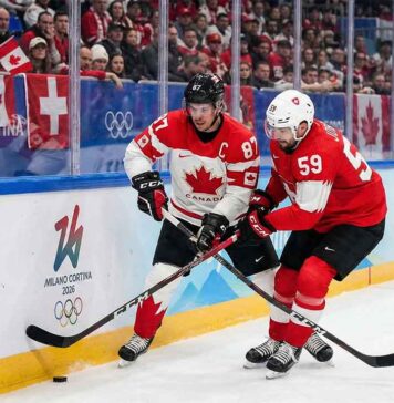Team Canada captain Sidney Crosby (87) and Team Switzerland captain Roman Josi (59) battle fiercely for possession of the puck along the boards during a preliminary round men's hockey game at the 2026 Milano Cortina Winter Olympics.