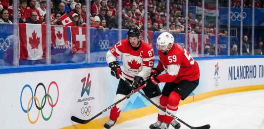 Team Canada captain Sidney Crosby (87) and Team Switzerland captain Roman Josi (59) battle fiercely for possession of the puck along the boards during a preliminary round men's hockey game at the 2026 Milano Cortina Winter Olympics.