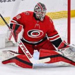 Carolina Hurricanes goaltender Jordan Binnington, wearing a red number 50 jersey and custom red, white, and black pads, positioned in a butterfly stance in front of the net.