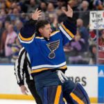 St. Louis Blues goaltender Jordan Binnington celebrates wildly on the ice with arms raised. In the background crowd behind the glass, a fan holds a sign that reads "The Habs want you Jordan!", referencing trade rumors connecting him to the Montreal Canadiens.