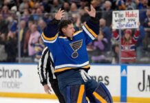St. Louis Blues goaltender Jordan Binnington celebrates wildly on the ice with arms raised. In the background crowd behind the glass, a fan holds a sign that reads "The Habs want you Jordan!", referencing trade rumors connecting him to the Montreal Canadiens.