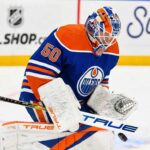 A photorealistic mock-up depicting St. Louis Blues goaltender Jordan Binnington wearing a full Edmonton Oilers uniform, including jersey #50 and custom customized pads, making a stick save. This image illustrates intensifying NHL trade rumors linking Binnington to the Oilers ahead of the deadline.