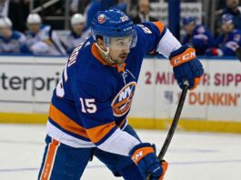 St. Louis Blues forward Jordan Kyrou is pictured in a New York Islanders blue home uniform, number 15, taking a shot during a hockey game.