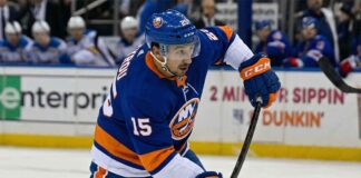 St. Louis Blues forward Jordan Kyrou is pictured in a New York Islanders blue home uniform, number 15, taking a shot during a hockey game.