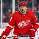 Detroit Red Wings defenseman Justin Faulk, wearing the red home jersey with number 72 and a red helmet, stands on the ice holding his stick during a game.