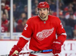 Detroit Red Wings defenseman Justin Faulk, wearing the red home jersey with number 72 and a red helmet, stands on the ice holding his stick during a game.