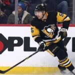 Pittsburgh Penguins defenseman Luke Schenn wearing the team's black home uniform and helmet, skating on the ice and looking intently forward during a game.