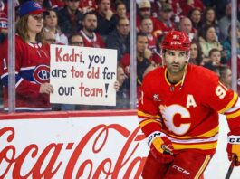 Calgary Flames center Nazem Kadri skates past a female Montreal Canadiens fan holding a handwritten sign that reads "Kadri, you are too old for our team!" during an NHL game.