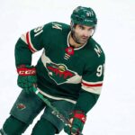 Minnesota Wild forward Nazem Kadri (91) skating on the ice wearing the team's forest green home jersey, breezers, socks, and helmet while holding his hockey stick.