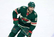 Minnesota Wild forward Nazem Kadri (91) skating on the ice wearing the team's forest green home jersey, breezers, socks, and helmet while holding his hockey stick.