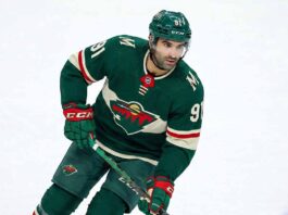 Minnesota Wild forward Nazem Kadri (91) skating on the ice wearing the team's forest green home jersey, breezers, socks, and helmet while holding his hockey stick.