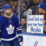 Toronto Maple Leafs forward Nicolas Roy (#55) skates past the boards during a game, looking towards a female fan behind the glass who is holding a handwritten sign that reads, "Good luck on your new team Nicolas."