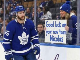 Toronto Maple Leafs forward Nicolas Roy (#55) skates past the boards during a game, looking towards a female fan behind the glass who is holding a handwritten sign that reads, "Good luck on your new team Nicolas."