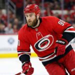 Nashville Predators center Ryan O'Reilly depicted in a red Carolina Hurricanes home uniform, skating with a puck during an NHL game.