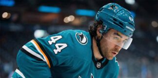 Kiefer Sherwood, wearing a teal San Jose Sharks uniform, looks over his shoulder on the ice amidst growing NHL trade deadline rumors regarding his future with the struggling team.
