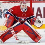 NHL goaltender Sergei Bobrovsky, wearing a red, white, and blue Montreal Canadiens uniform, pads, and mask, is in a butterfly stance on the ice in front of the net. His eyes are focused on a puck sliding on the ice to his right.