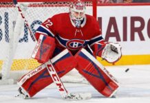 NHL goaltender Sergei Bobrovsky, wearing a red, white, and blue Montreal Canadiens uniform, pads, and mask, is in a butterfly stance on the ice in front of the net. His eyes are focused on a puck sliding on the ice to his right.
