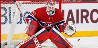 NHL goaltender Sergei Bobrovsky, wearing a red, white, and blue Montreal Canadiens uniform, pads, and mask, is in a butterfly stance on the ice in front of the net. His eyes are focused on a puck sliding on the ice to his right.