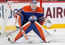 Sergei Bobrovsky crouched in a butterfly stance guarding the net, wearing a full Edmonton Oilers goaltender uniform including a blue and orange jersey, custom-painted mask, and matching pads with a puck visible near his glove.