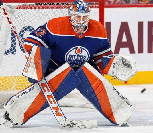 Sergei Bobrovsky crouched in a butterfly stance guarding the net, wearing a full Edmonton Oilers goaltender uniform including a blue and orange jersey, custom-painted mask, and matching pads with a puck visible near his glove.