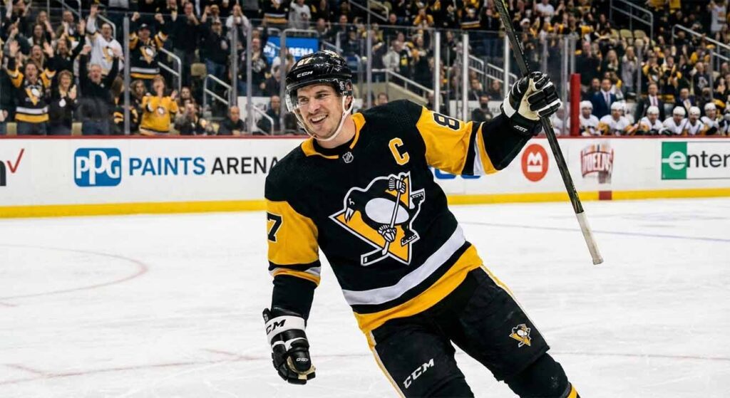Pittsburgh Penguins captain Sidney Crosby smiles and raises his stick in celebration on the ice during a game at PPG Paints Arena.