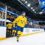 Team Sweden captain Gabriel Landeskog, wearing the yellow Tre Kronor jersey with the 'C', skates out of the tunnel leading his teammates onto the ice for the Milano Cortina 2026 Winter Olympics group stage game against Team Italy.